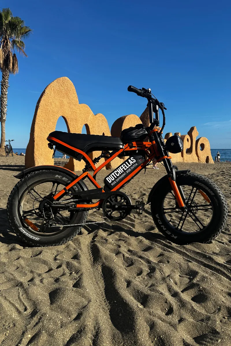 An orange DutchFellas fatbike parked on a Málaga beach
